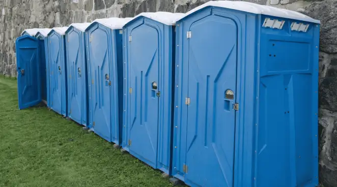 Row of blue portable toilets lined up on grass against a stone wall for event sanitation in Rockford, IL