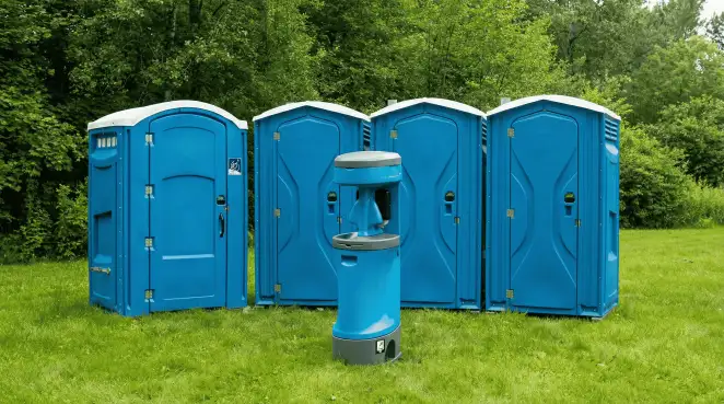 Four blue portable toilets and a matching hand washing station on grass near trees, a common sight at local outdoor events in Rockford, IL