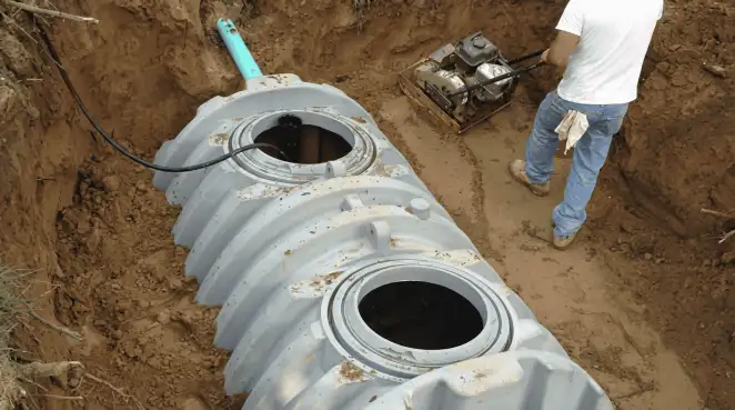 Septic tank installation showing a technician compacting soil around a new poly septic tank in an excavation pit in Rockford, IL